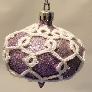 Purple glitter ornament covered with intricate white hand-tatted lace in a snowflake lattice pattern.