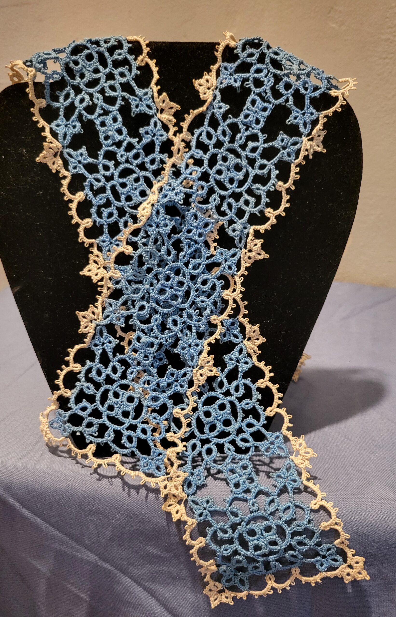 Long handmade blue and cream tatted lace scarf with intricate floral motifs and delicate picot edging displayed on a black bust stand.