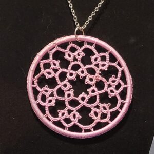 Round blush pink hand-tatted lace medallion pendant on an 18-inch silver-tone chain displayed against a black background.