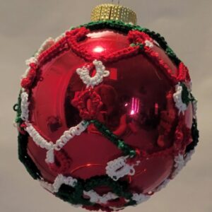Glossy red ornament decorated with intricate hand-tatted lace in red, green, and white holiday colors.
