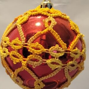 Deep red glass ornament decorated with intricate golden yellow hand-tatted lace in looping floral patterns.