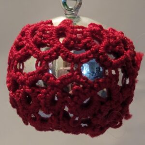 Small silver ornament wrapped in intricate deep red hand-tatted lace with an openwork floral pattern.