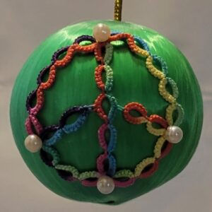 Green ornament decorated with rainbow-colored hand-tatted lace garlands and pearl bead accents.
