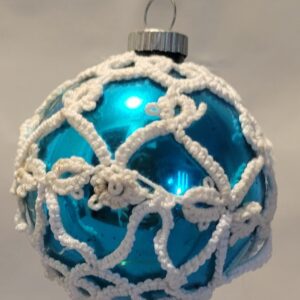 Bright blue ornament covered with intricate white hand-tatted lace in flowing snowflake-like patterns.