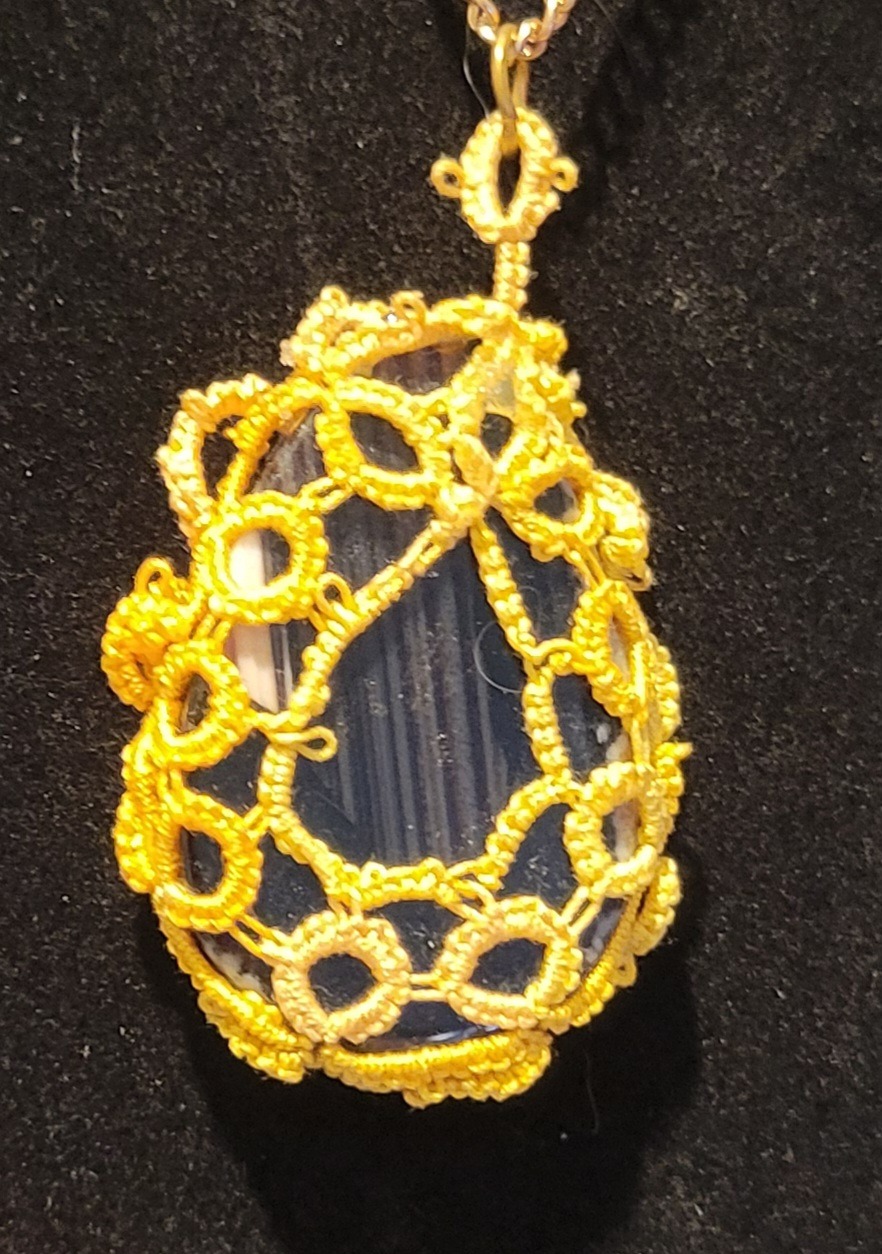 Yellow lace surrounds a clear, teardrop-shaped pendant on a black background
