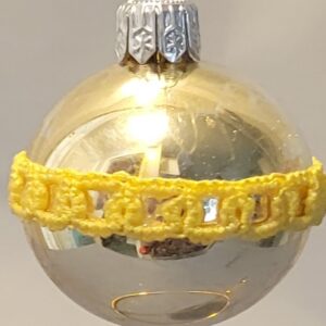 Silver reflective ornament wrapped with a narrow band of intricate golden yellow hand-tatted lace.
