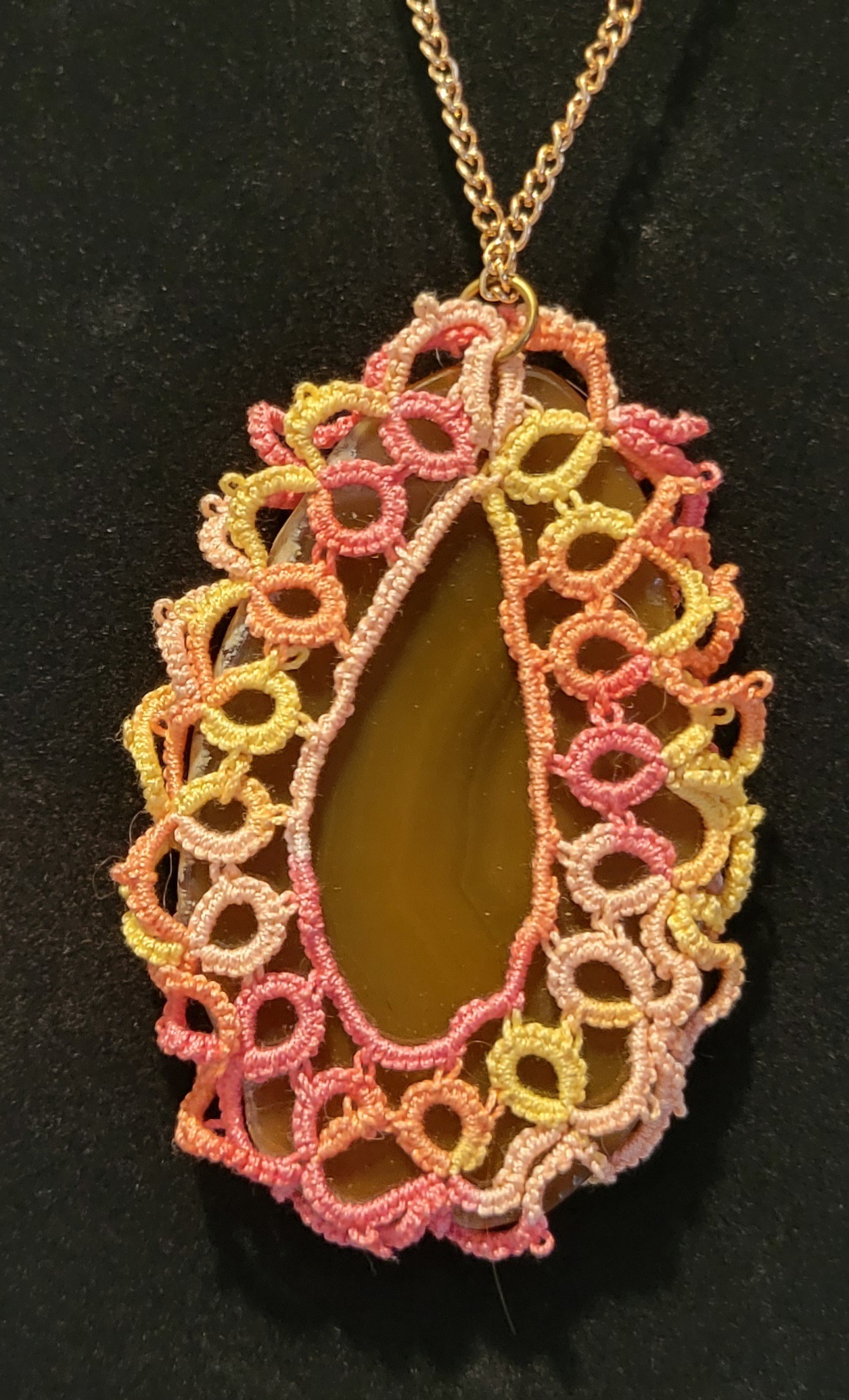 A colorful, intricately knotted lace pendant encases a smooth