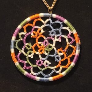 Round multicolor hand-tatted lace medallion pendant in autumn tones on an 18-inch gold-tone chain displayed against a black background.
