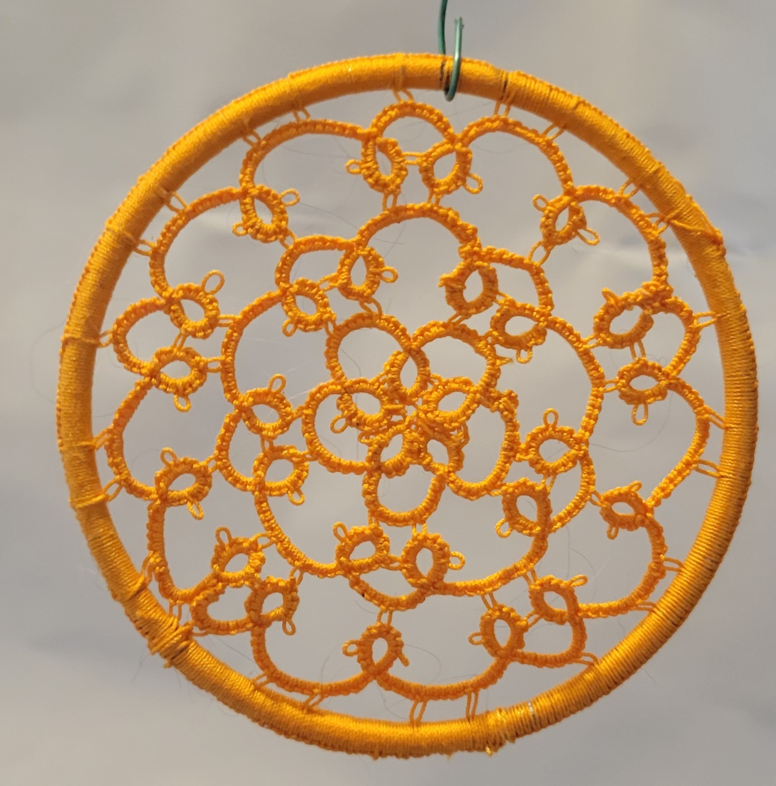 Hand-tatted marigold orange mandala with intricate floral lacework suspended inside a matching wrapped 4-inch hoop.
