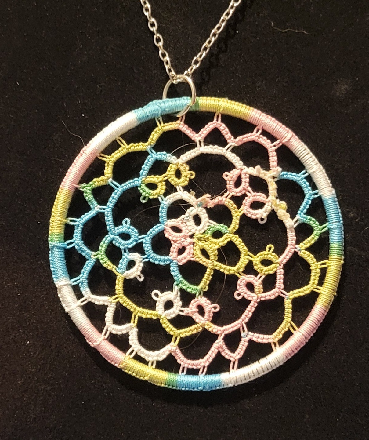 Round pastel multicolor hand-tatted lace medallion pendant on an 18-inch silver-tone chain displayed against a black background.