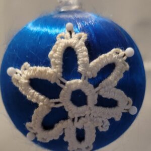 Blue satin ornament decorated with an white hand-tatted snowflake lace motif accented with white pins.