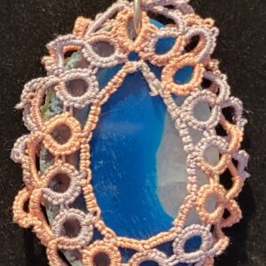 Blue agate pendant wrapped in intricate lace-like embroidery with pastel colors