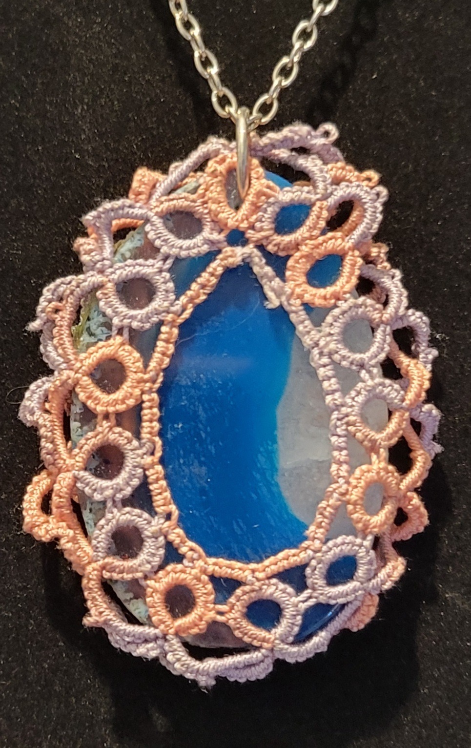 Blue agate pendant wrapped in intricate lace-like embroidery with pastel colors