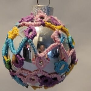 Small silver ornament decorated with pastel rainbow hand-tatted lace in looping candy-like patterns.