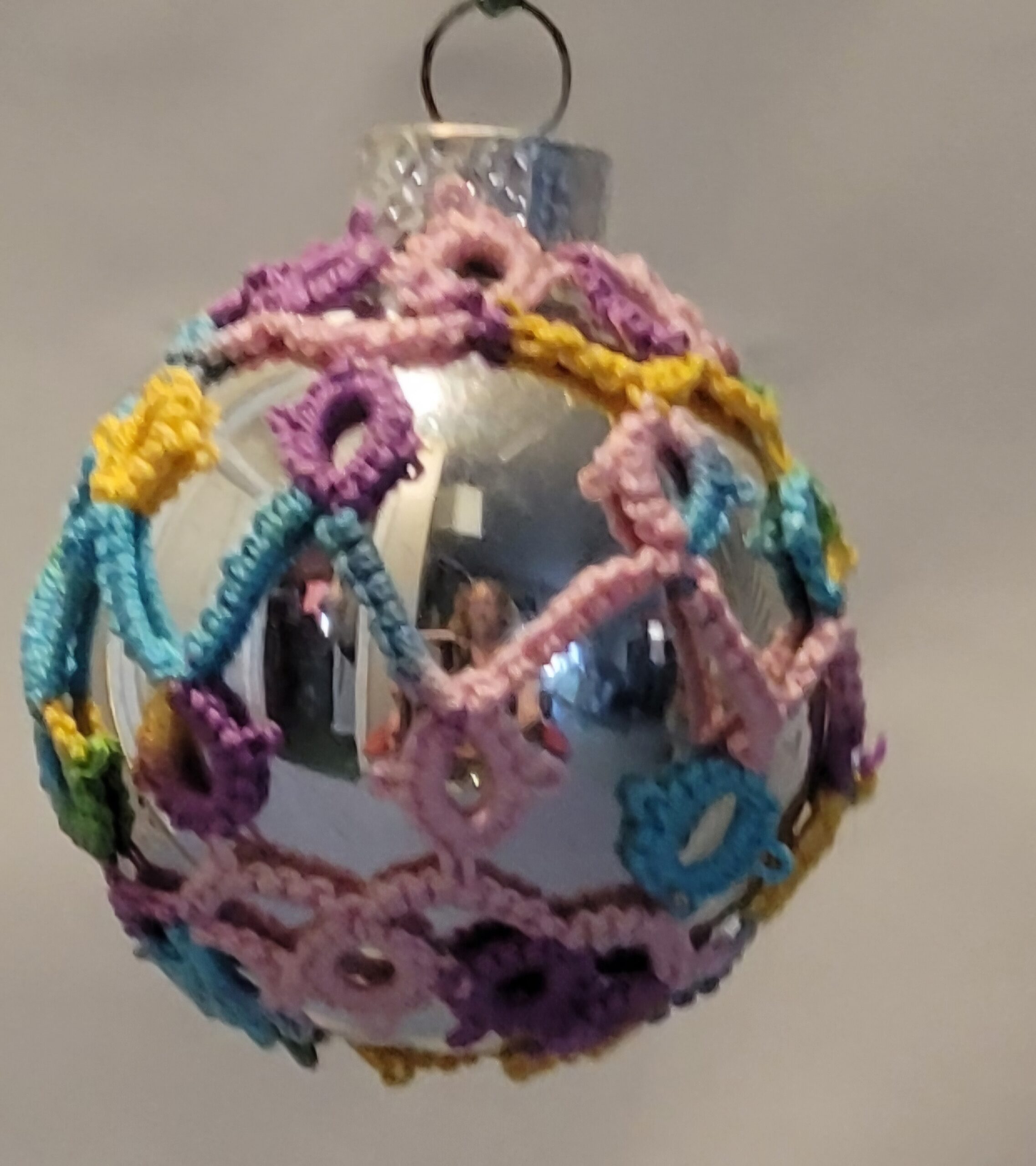 Small silver ornament decorated with pastel rainbow hand-tatted lace in looping candy-like patterns.