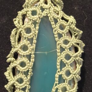 Aquamarine pendant encased in intricate green lace, hanging from a chain