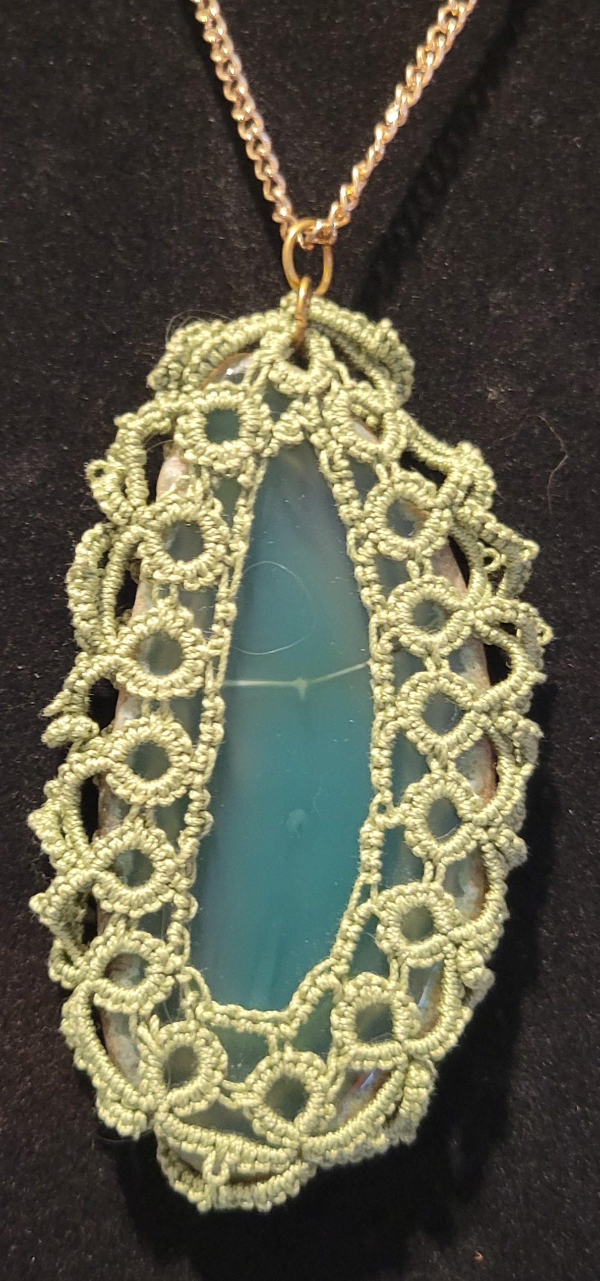 Aquamarine pendant encased in intricate green lace, hanging from a chain