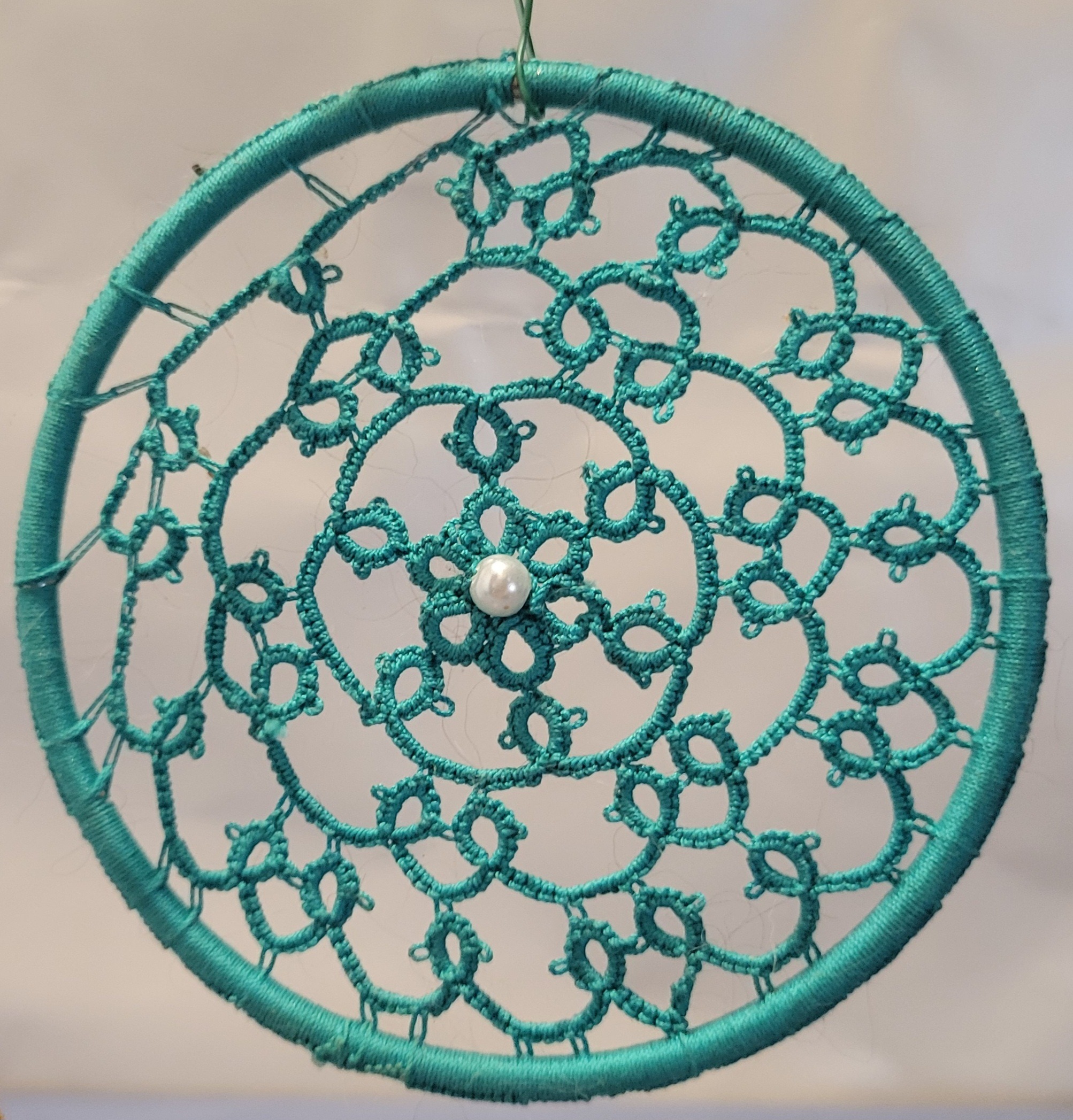 Hand-tatted seafoam teal mandala with intricate lacework and a pearl center suspended inside a matching wrapped 4-inch hoop.designs