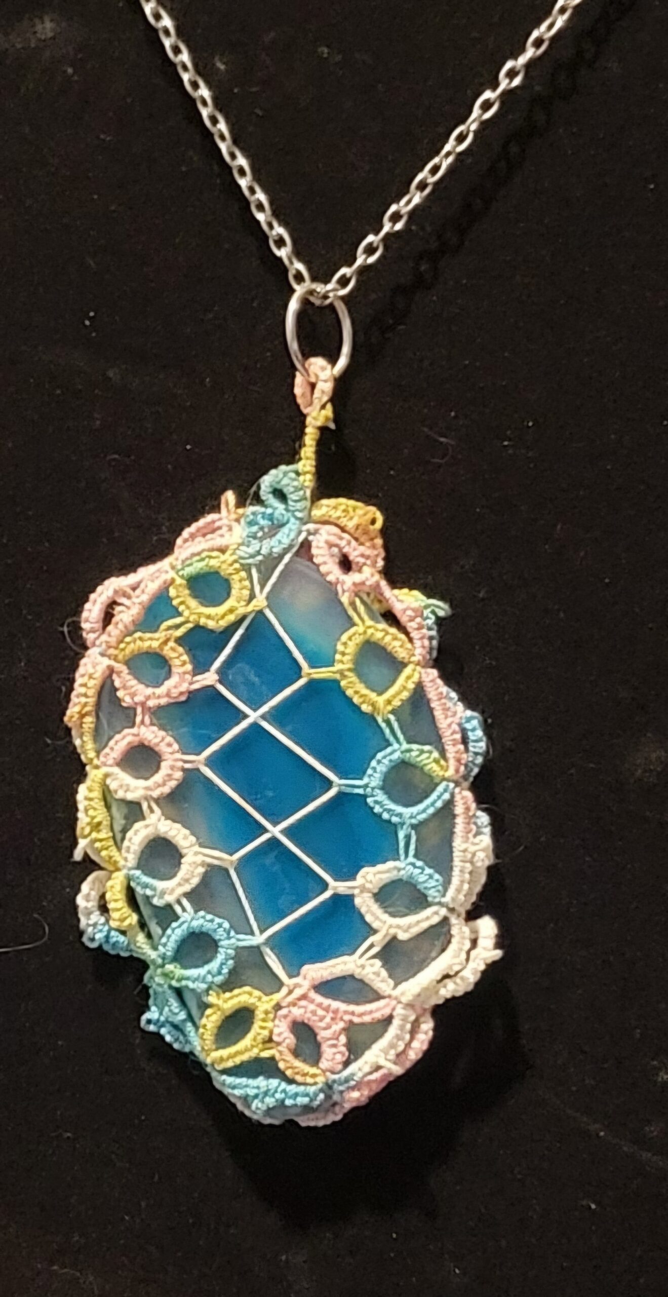 Blue agate pendant wrapped in pastel hand-tatted lace on a 20-inch silver-tone chain displayed against a black background.