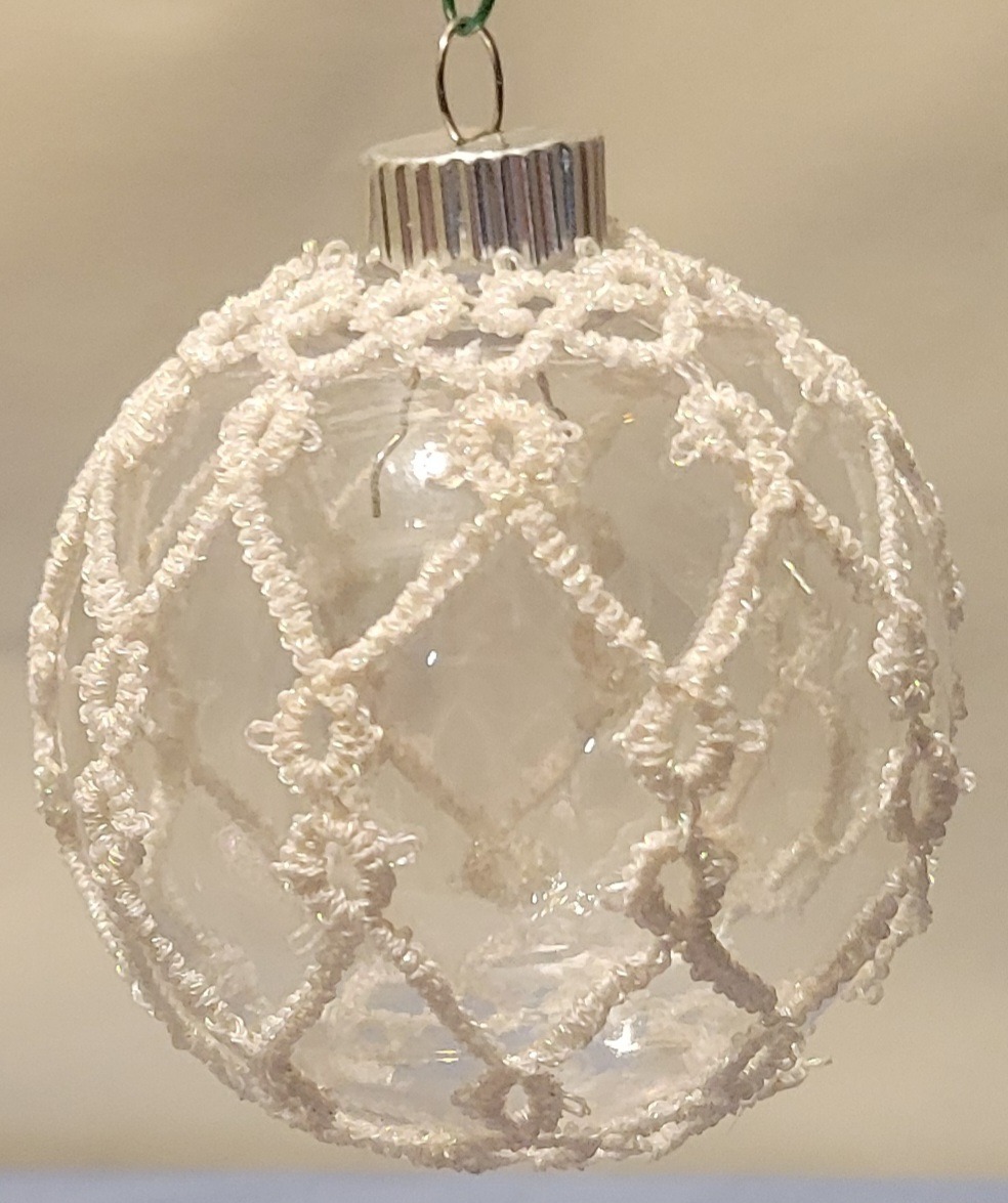 Clear glass ornament covered with delicate white hand-tatted lace in an intricate frosted lattice pattern.