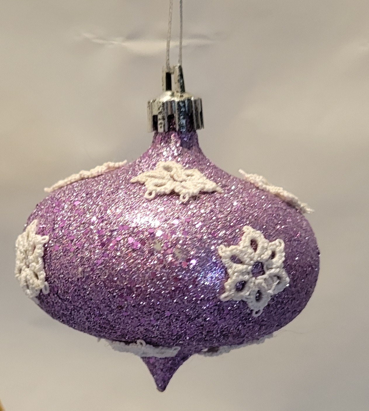 Lavender glitter finial ornament decorated with delicate ivory hand-tatted snowflake motifs.