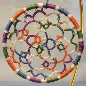 Hand-tatted multicolor lace mandala in wildflower-inspired shades suspended inside a wrapped 4-inch hoop with intricate floral-style tatting details.