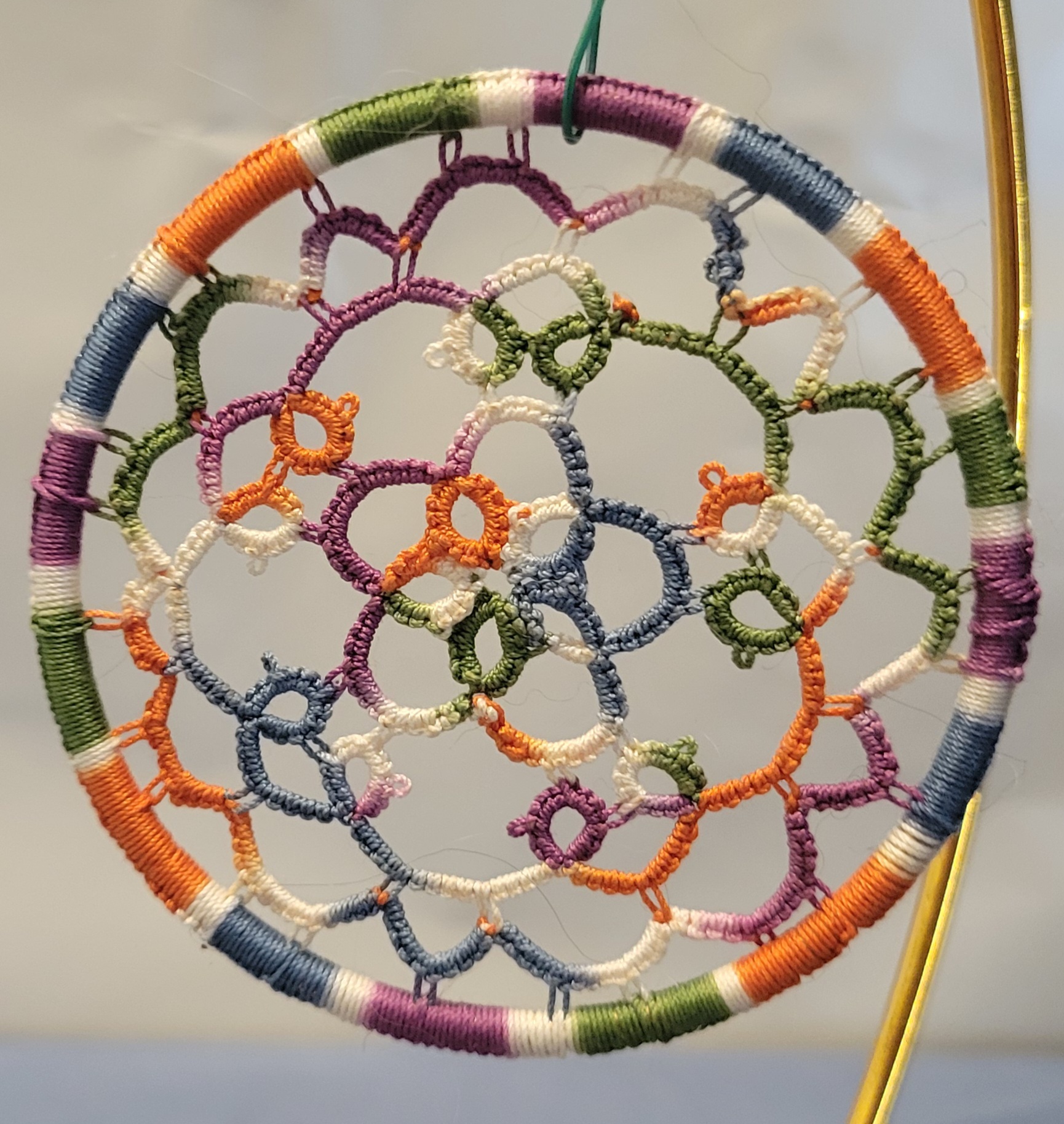 Hand-tatted multicolor lace mandala in wildflower-inspired shades suspended inside a wrapped 4-inch hoop with intricate floral-style tatting details.