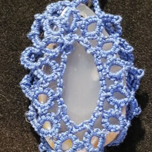 Pale agate pendant wrapped in cobalt blue hand-tatted lace on a 20-inch pewter-tone chain displayed against a black background.