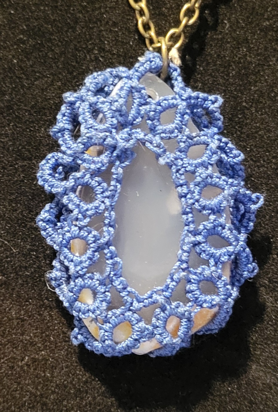 Pale agate pendant wrapped in cobalt blue hand-tatted lace on a 20-inch pewter-tone chain displayed against a black background.