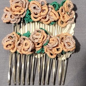 Pair of silver-tone hair combs decorated with handmade tatted lace flowers in peach and taupe shades with green leaves on a gray fabric background.