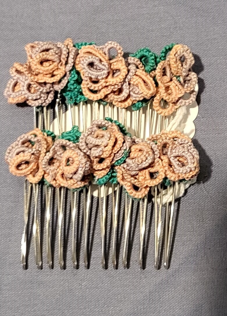 Pair of silver-tone hair combs decorated with handmade tatted lace flowers in peach and taupe shades with green leaves on a gray fabric background.