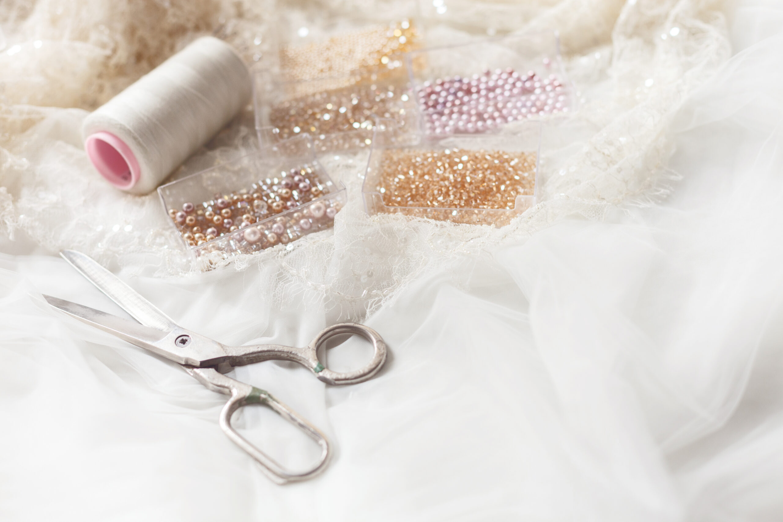 Scissors, a spool of white thread, and containers of colorful beads