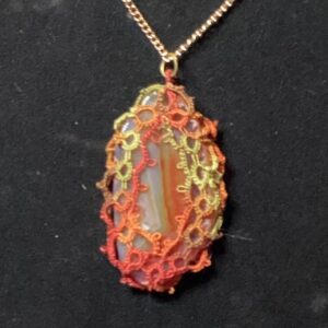 Banded agate pendant wrapped in red, orange, and green hand-tatted lace on a 20-inch chain displayed against a dark background.