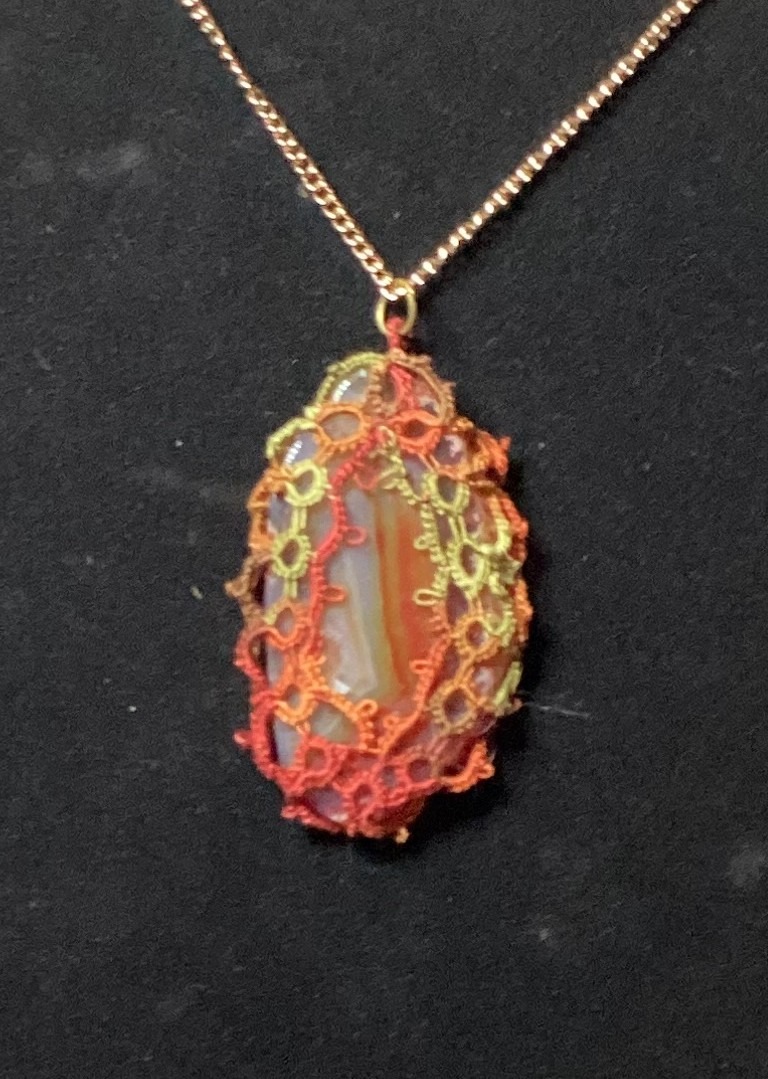 Banded agate pendant wrapped in red, orange, and green hand-tatted lace on a 20-inch chain displayed against a dark background.