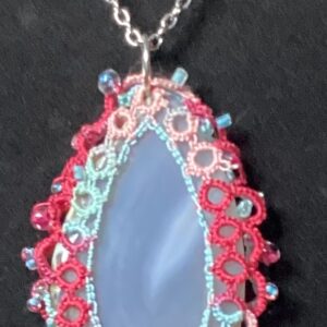 Blue agate pendant wrapped in colorful hand-tatted lace with bead accents on an 18-inch chain displayed against a dark background.