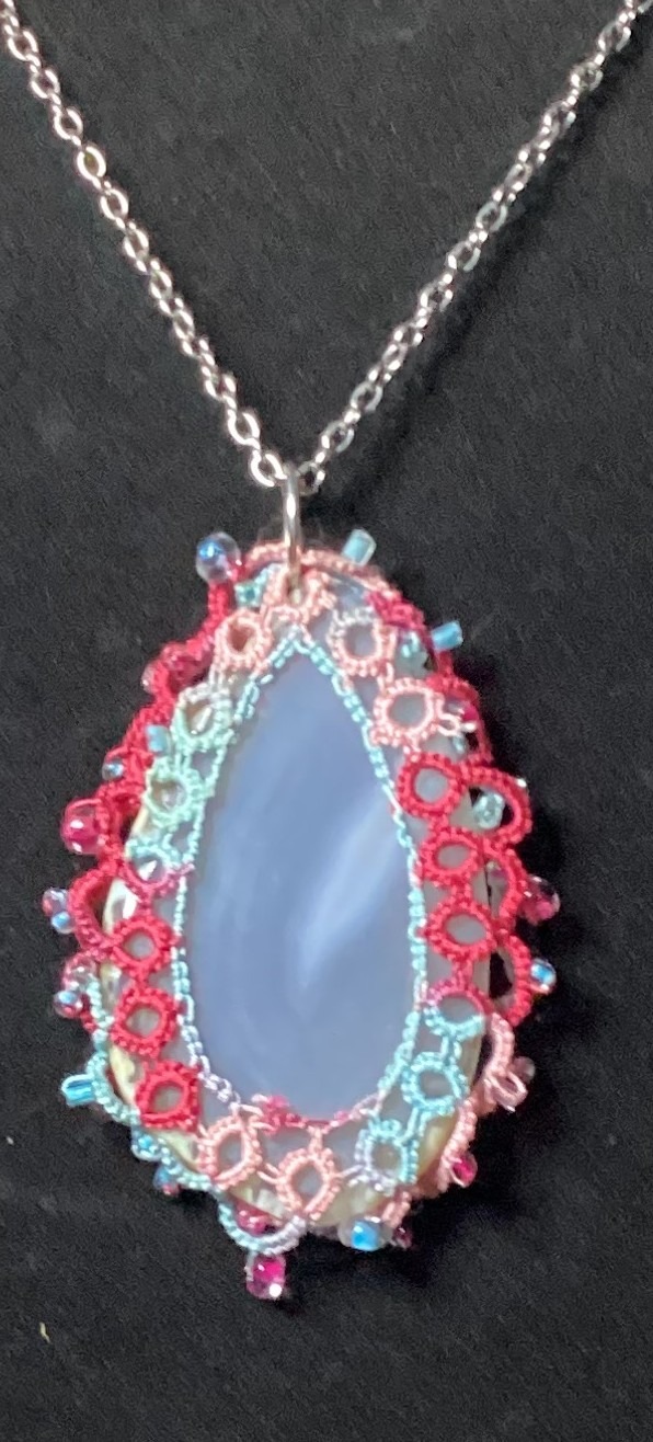Blue agate pendant wrapped in colorful hand-tatted lace with bead accents on an 18-inch chain displayed against a dark background.