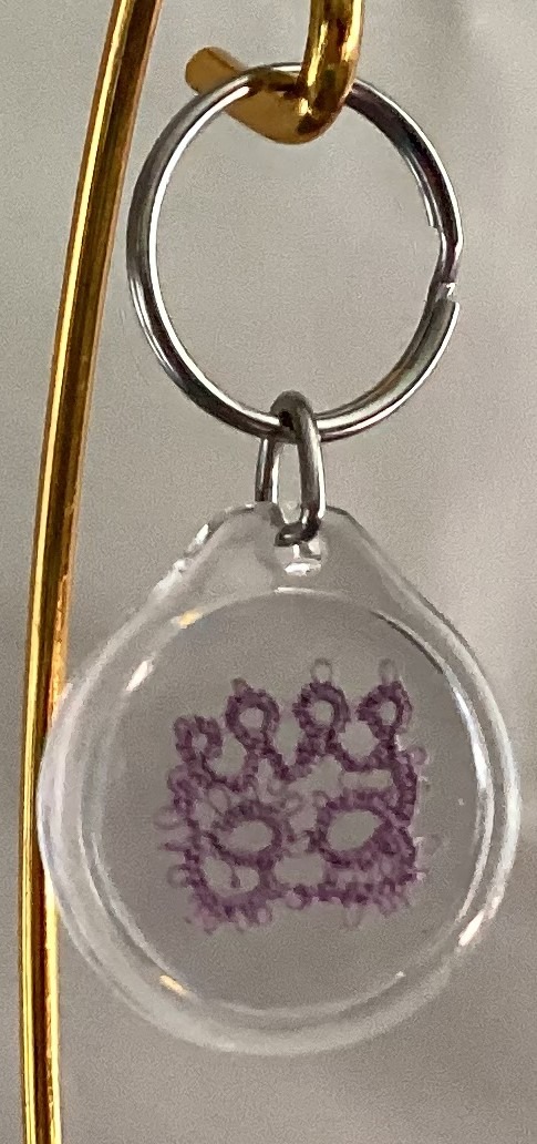 Clear acrylic keychain featuring a lavender tatted paw print design with silver key ring.