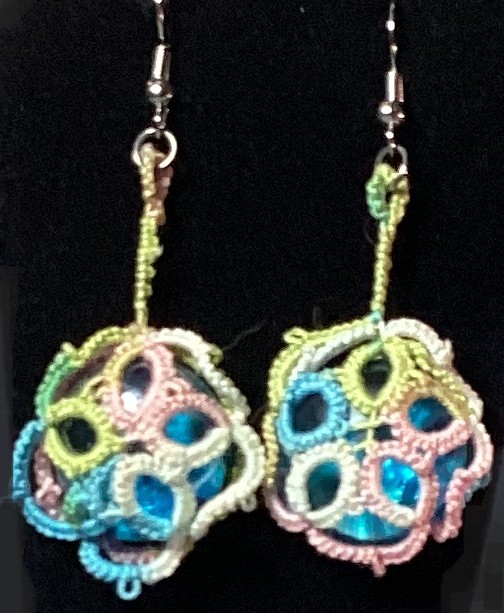Handmade pastel rainbow tatted earrings with blue iridescent cabochons and silver-tone hooks against a black background.
