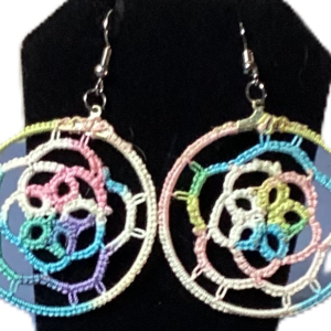 Handmade pastel rainbow tatted hoop earrings with spiral lacework and silver-tone hooks displayed against a black background.