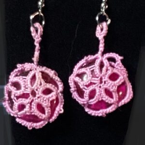 Handmade pink tatted earrings with raspberry-pink cabochons and silver-tone hooks displayed against a black background.