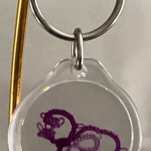 Clear acrylic keychain featuring a violet and lavender tatted bird design with silver key ring.