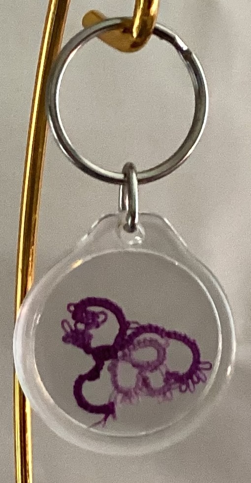 Clear acrylic keychain featuring a violet and lavender tatted bird design with silver key ring.