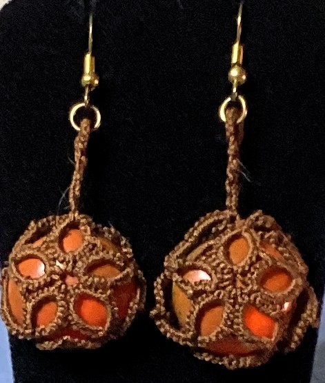 Handmade brown tatted earrings with amber-orange cabochons and gold-tone hooks against a black background.