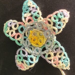 Hand-tatted floral hair pin with pastel lace petals in aqua, pink, lavender, and cream surrounding a yellow flower center, mounted on a metal hair pin, 3 inches in diameter.