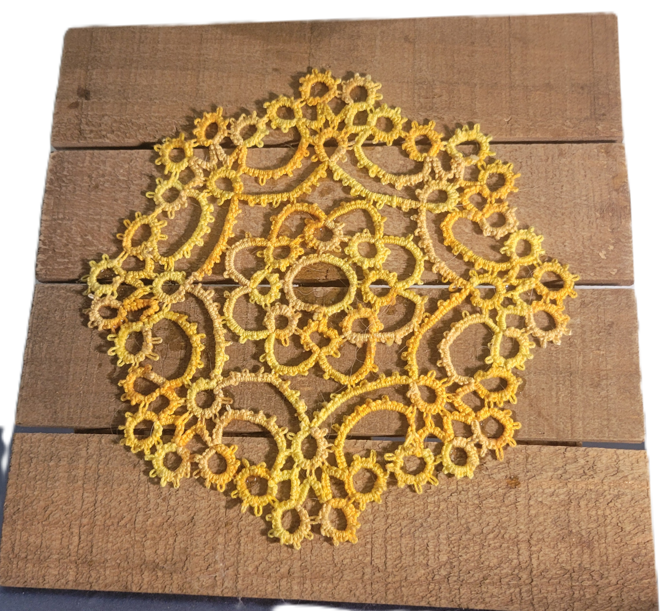 Handmade golden yellow needle-tatted lace doily with intricate floral and circular motifs in an 8-inch square design, displayed on a rustic wooden background.