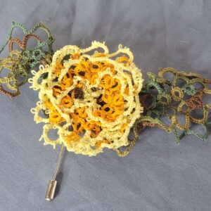 Hand-tatted golden flower hat and lapel pin with cream petals and variegated green leaves on a silver pin back.