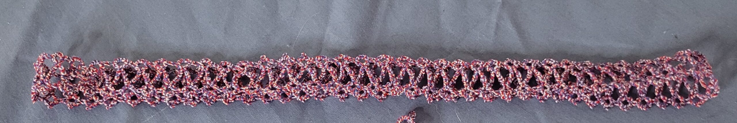 Hand-tatted patriotic lace hat band in variegated red, white, and blue with an intricate openwork design.
