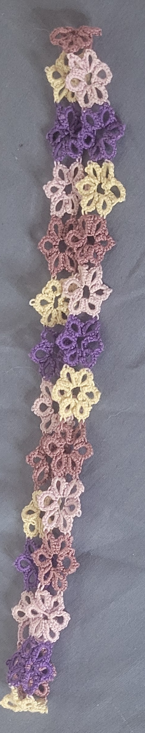 Hand-tatted floral lace hat band featuring purple, lavender, pink, mauve, and yellow flowers arranged in a continuous handmade design.
