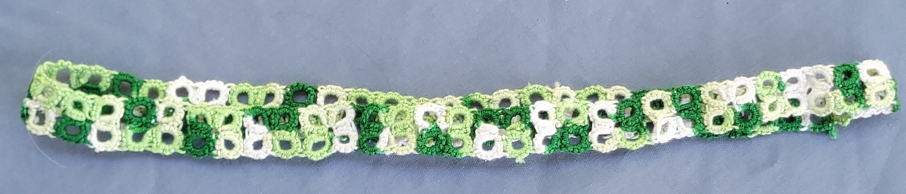Green, light green, and white hand-tatted lace hat band with intricate repeating pattern
