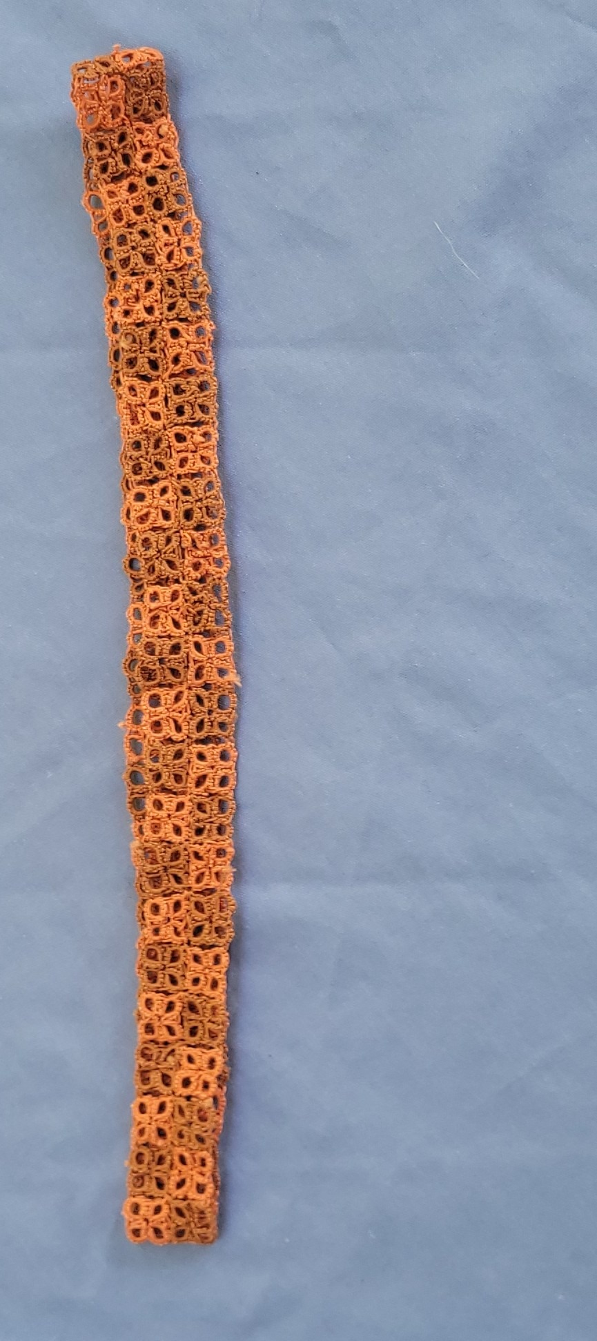 Rust-orange hand-tatted lace hat band displayed around a neutral-colored wide-brim hat outdoors